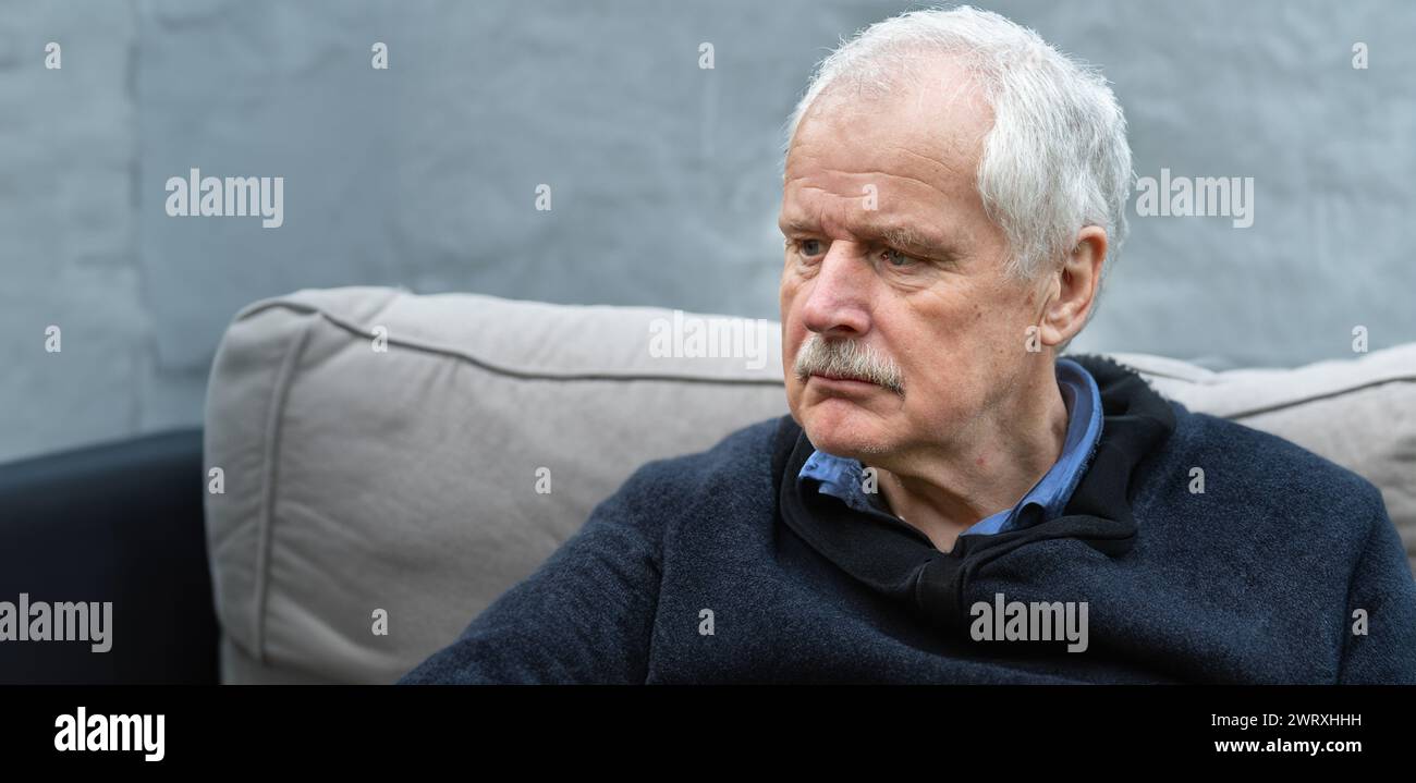Uomo anziano con una triste espressione seduto da solo sul divano. Simbolo di un uomo in lutto. Foto Stock