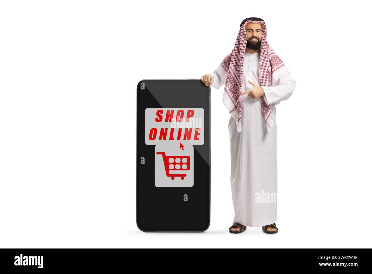 Uomo arabo saudita in abiti etnici in piedi accanto a un telefono cellulare con insegna dello shopping online isolata su sfondo bianco Foto Stock
