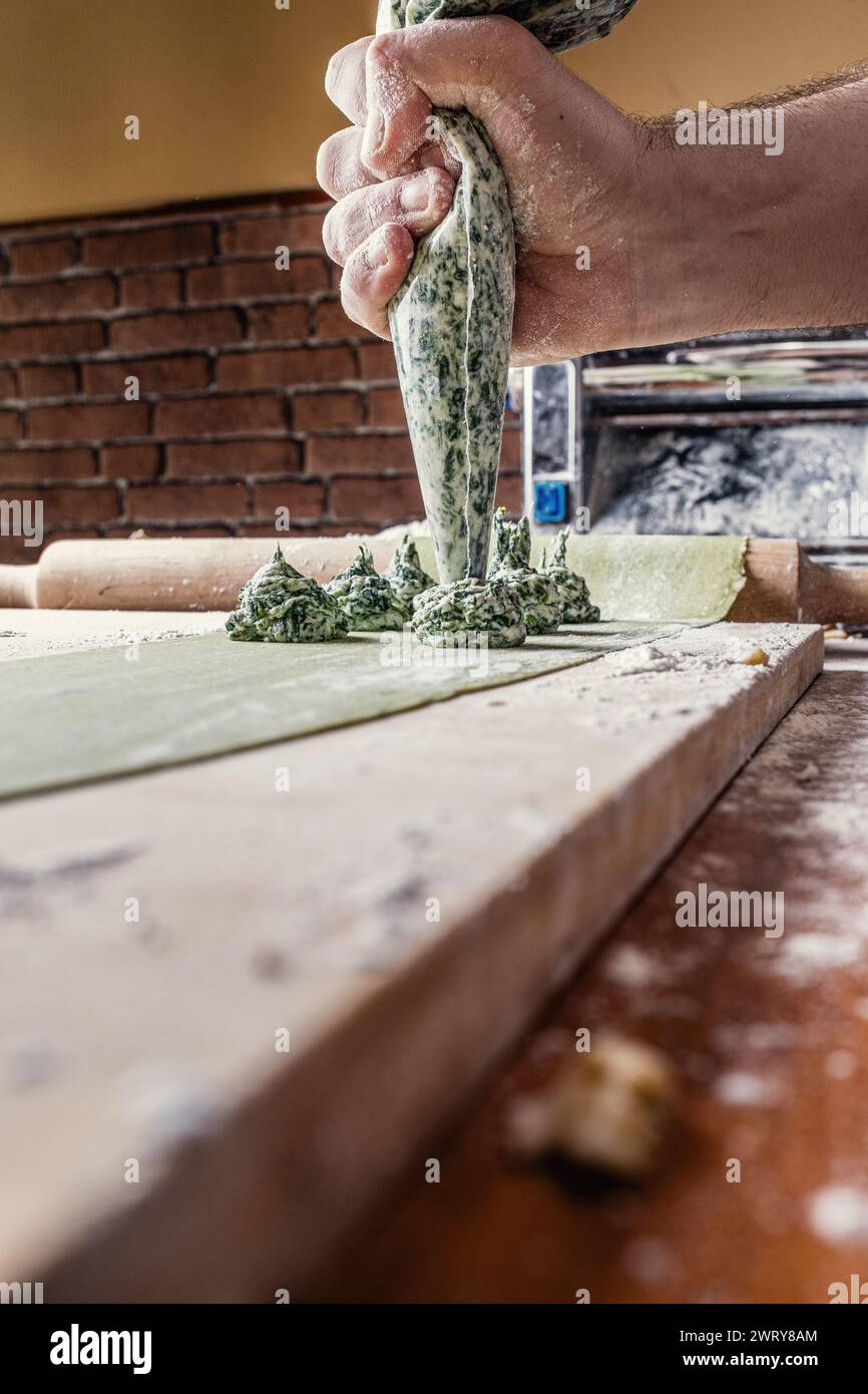 Primo piano della mano dello chef che prepara il ripieno di ravioli composto da un mix omogeneo di ricotta e spinaci. Foto Stock