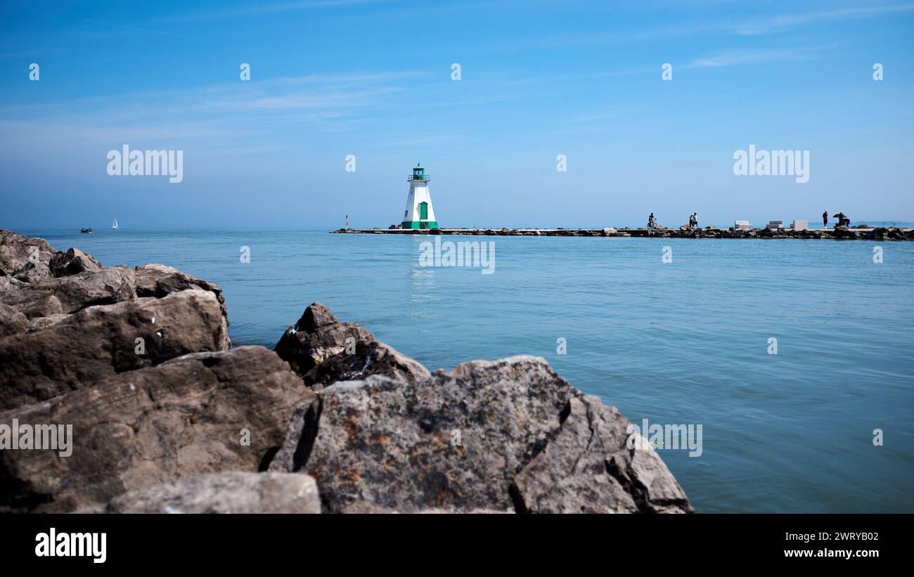 Storico faro fronte Port Dalhousie Range con rocce in primo piano e lago Ontario sullo sfondo. Cielo blu. Acqua blu. Foto Stock