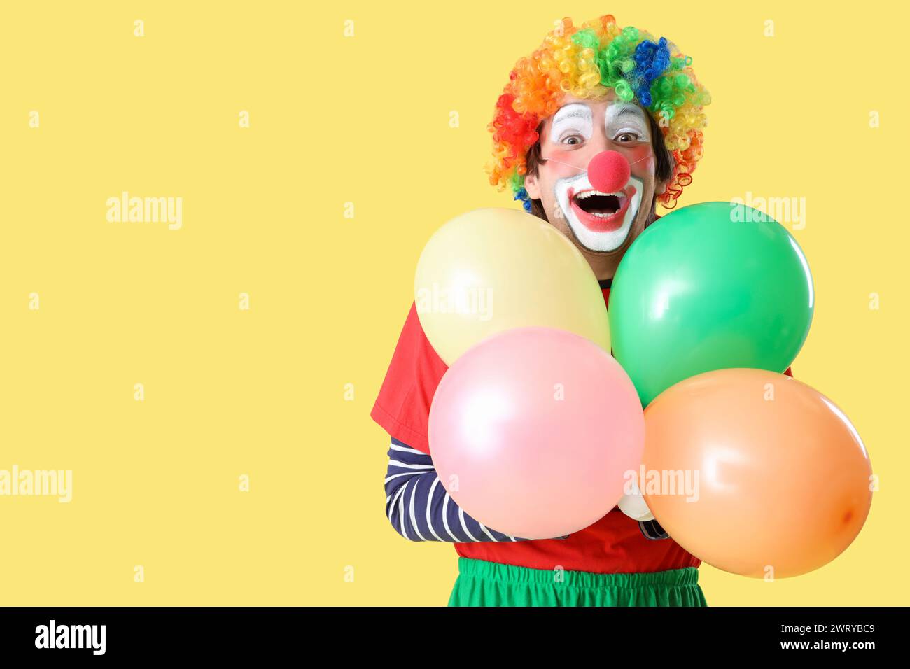 Ritratto del clown con palloncini su sfondo giallo. Festa del giorno dello scemo d'aprile Foto Stock