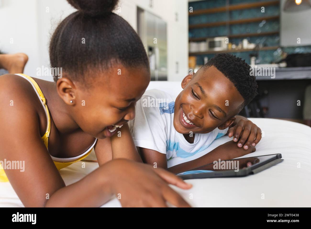 Un giovane fratello e una sorella afro-americana si fidanzano con un tablet sul divano di casa Foto Stock