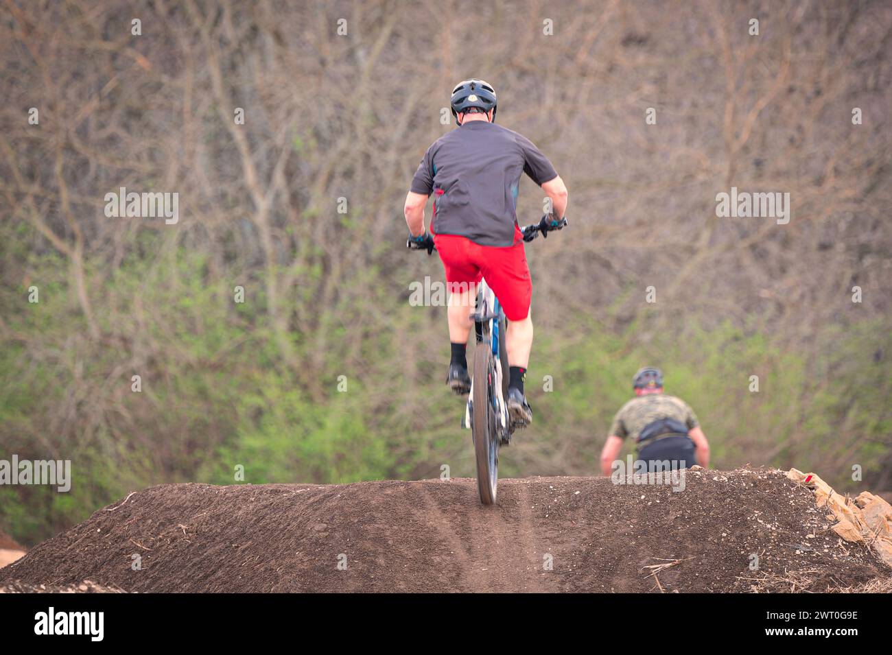 Una persona salta una moto da terra con un altro pilota sullo sfondo Foto Stock