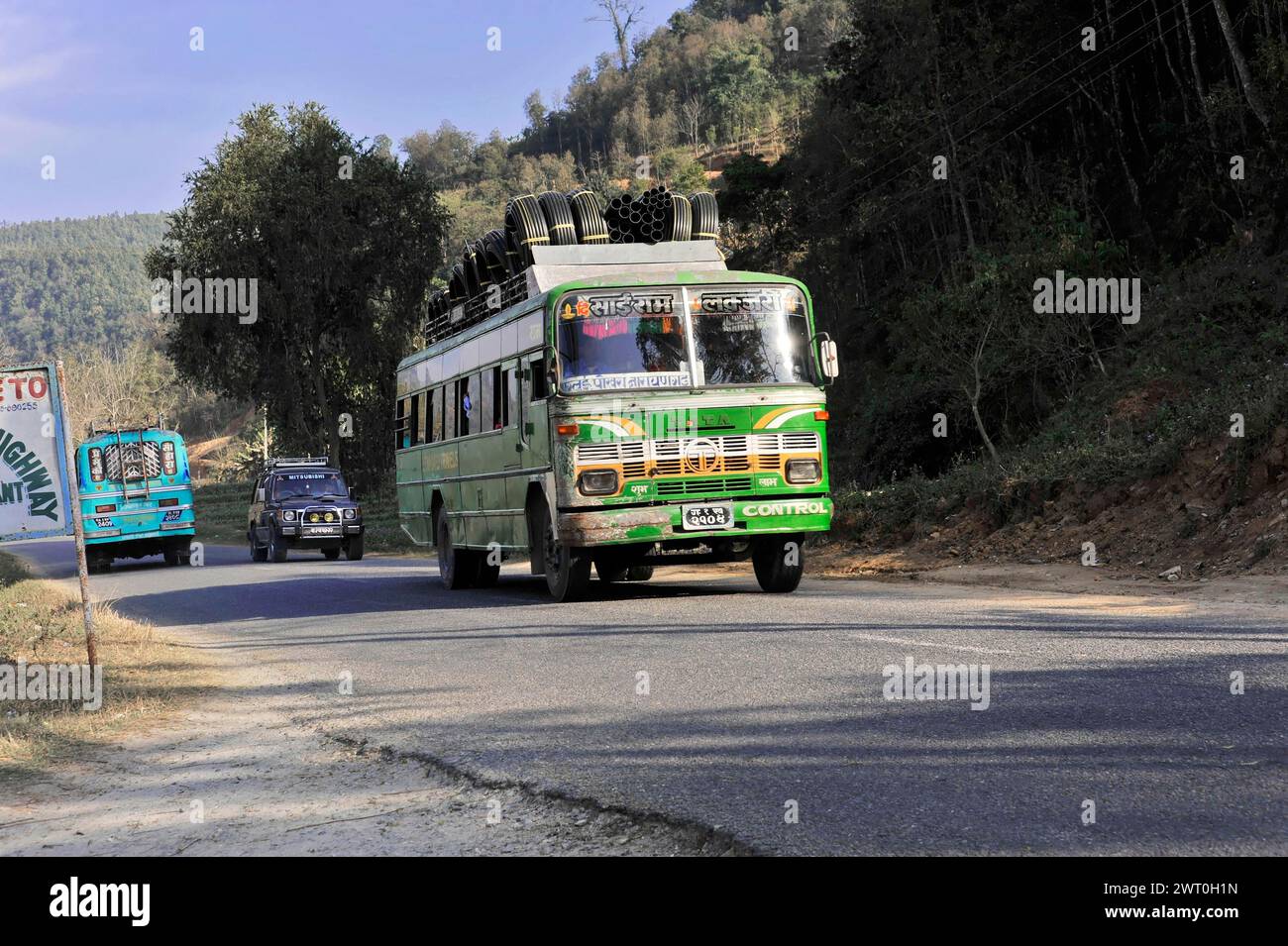 Autobus che viaggia su strada in un paesaggio collinare con alberi e cielo blu, Pokhara Valley, Pokhara, Nepal Foto Stock