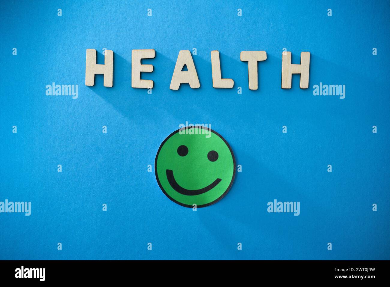 Sfondo sanitario generico con lettere ritagliate in legno e emoticon sorridente verde isolato su sfondo blu. Vista dall'alto Foto Stock