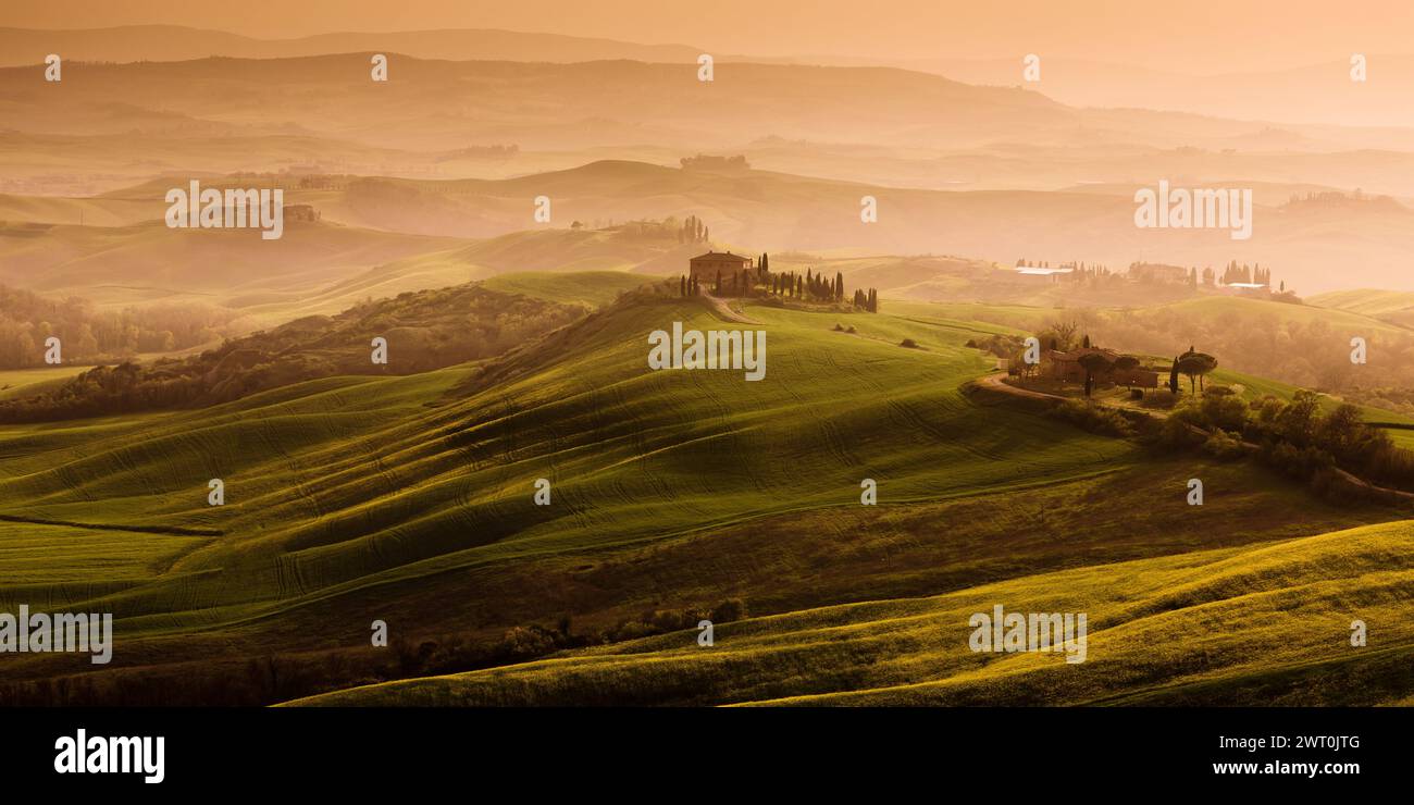 Un bellissimo paesaggio toscano nebbioso con una villa sulla cima di una collina e nebbia sullo sfondo durante il tramonto. Una bellissima destinazione di viaggio in Italia. Foto Stock
