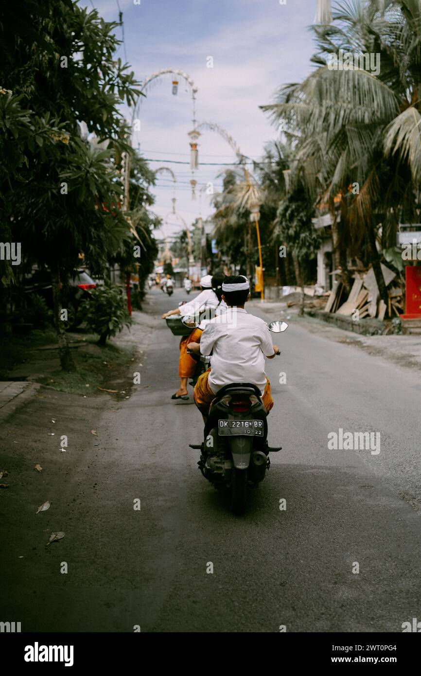 I balinesi in abiti nazionali percorrono la strada in moto. Foto Stock