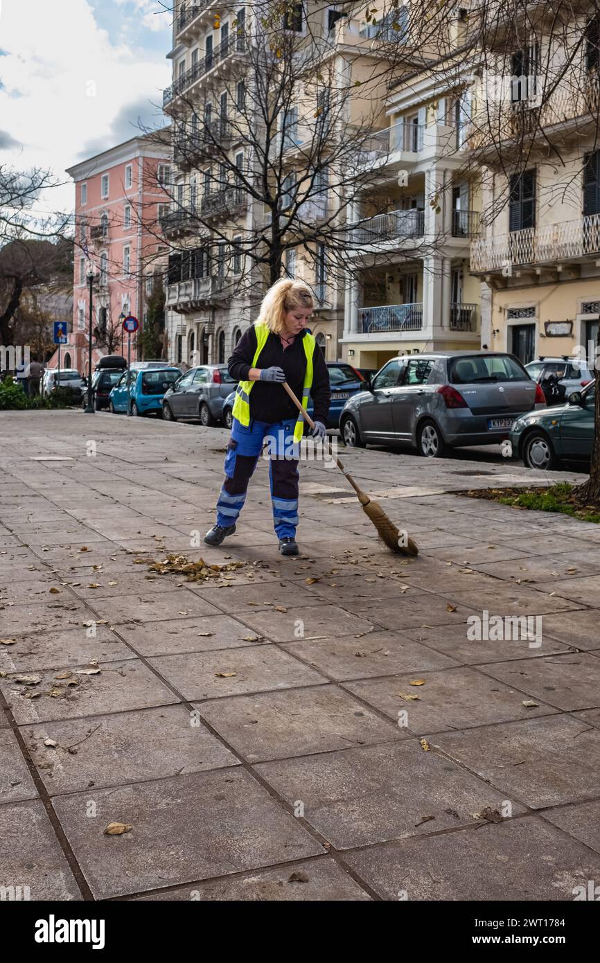 Processo di pulizia stradale urbana. Lavoratore con scopa. Pulitori stradali che spazzano le foglie cadute all'aperto il giorno autunnale. Ragazza di strada in città Foto Stock