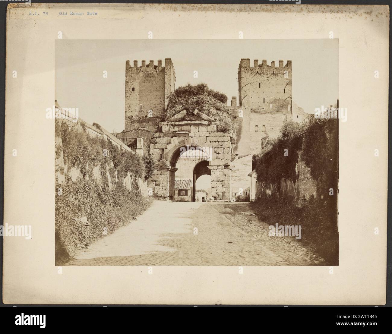 Arco di Druso. Sconosciuto, fotografo intorno al 1865-1880, una porta arcuata in pietra fiancheggiata da due torri di uguale altezza. La parte superiore di ogni torre è merlata. L'erba cresce in cima all'arco. Le pareti che costeggiano la strada che conduce all'arco sono ricoperte di erba e edera. (Recto, montaggio) in alto a sinistra, stampa blu su etichetta di carta: "B.I. 78 Old Roman Gate"; (verso, Mount) in alto a sinistra, inchiostro nero: "Old Roman Gate". Foto Stock