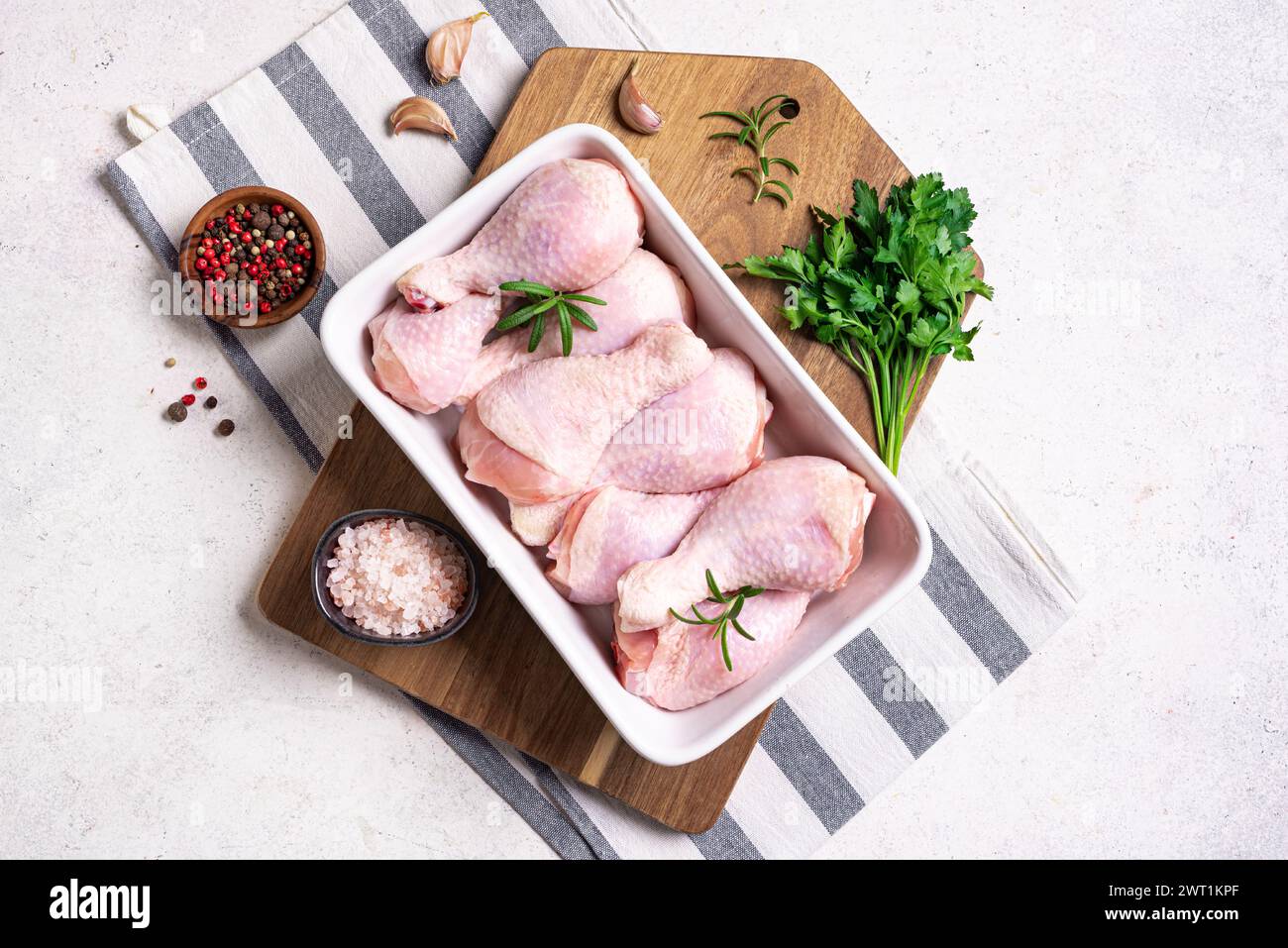 Cosce di pollo crude in teglia da forno con erbe, spezie e aglio pronte per la cottura in forno, sfondo bianco, vista dall'alto, spazio copia. Preparazione dell'organo grezzo Foto Stock