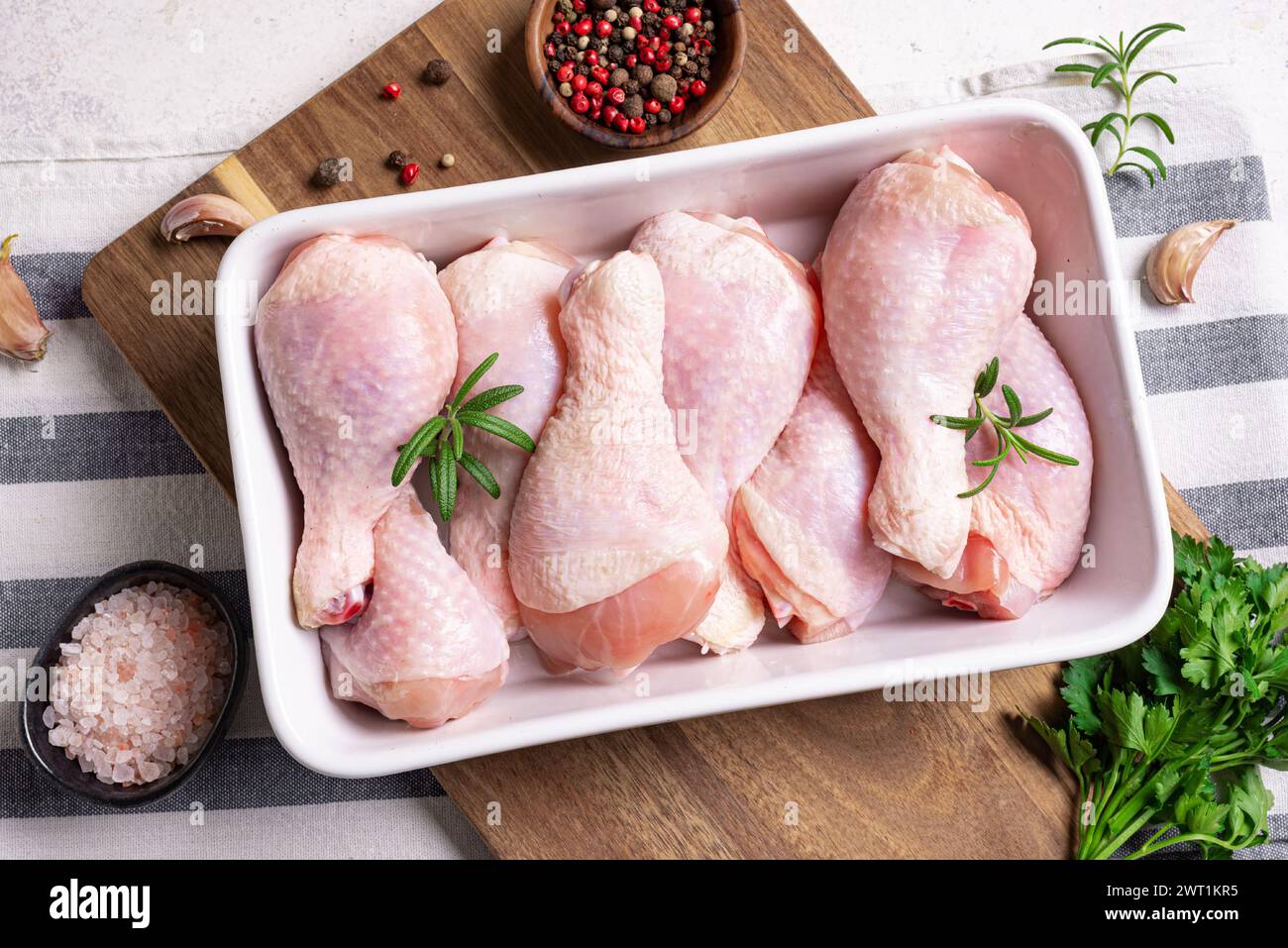 Cosce di pollo crude in teglia da forno con peperoni, rosmarino, prezzemolo e aglio pronte per la cottura su sfondo bianco, vista dall'alto, spazio copia. Preparazione ar Foto Stock