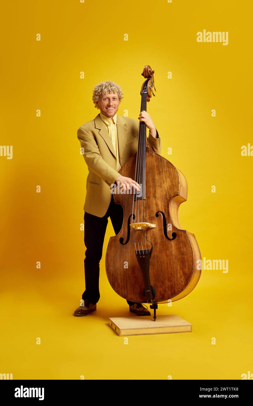 Uomo elegante in tuta che paga il contrabbasso, che esegue musica classica dal vivo su uno sfondo giallo brillante Foto Stock