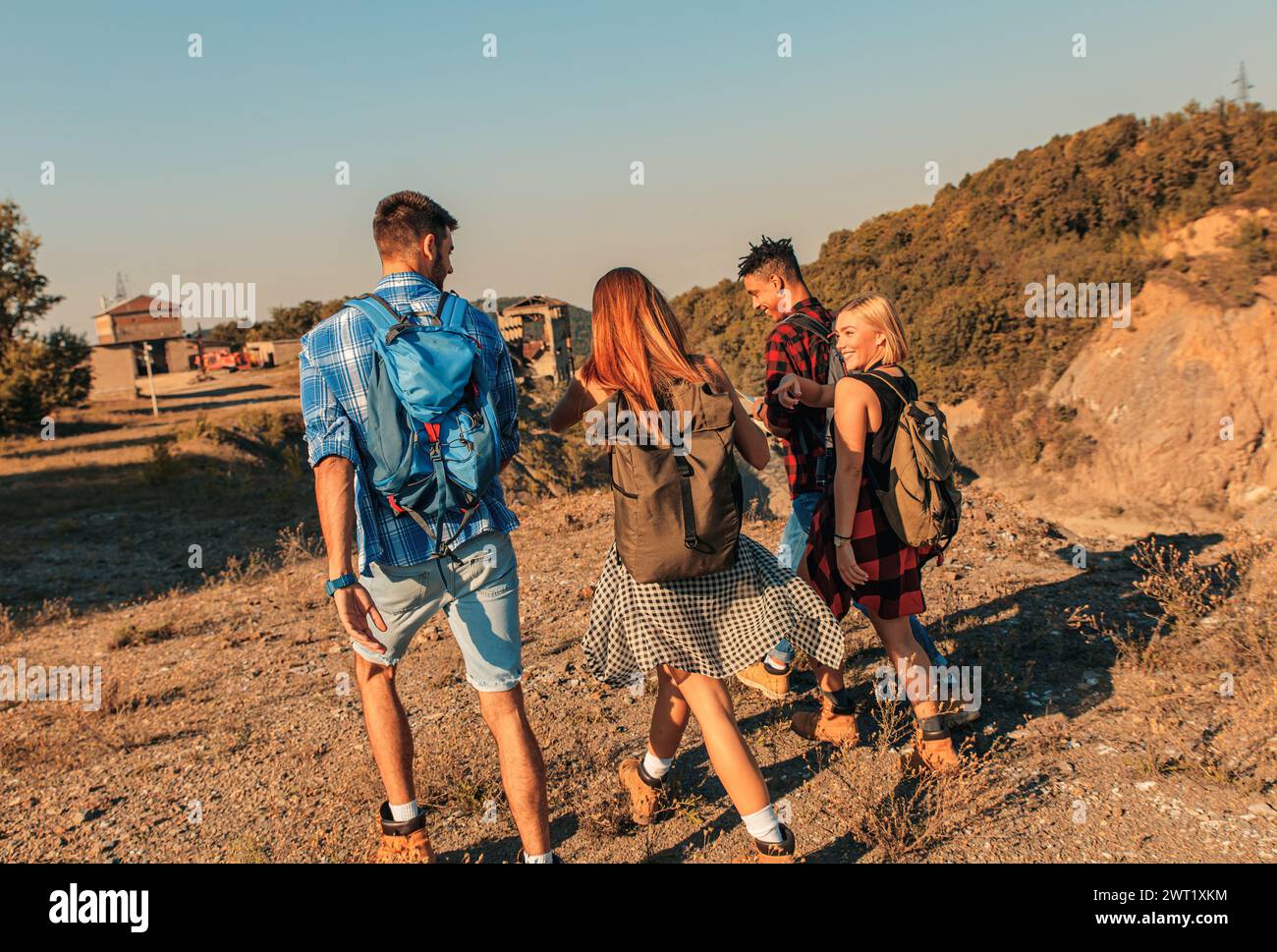 Gruppo di quattro amici che camminano insieme attraverso la campagna al tramonto. Foto Stock