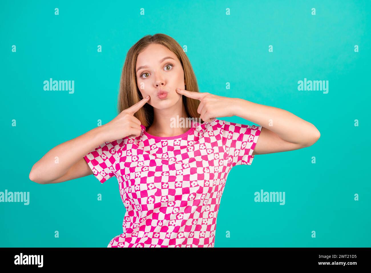 Ritratto fotografico di una bella ragazza adolescente dita punta guance labbra morbide indossa abiti rosa stampati alla moda isolati su sfondo di colore ciano Foto Stock