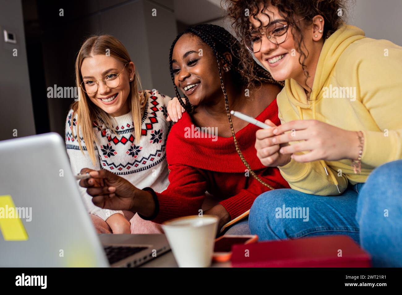 Diverse studentesse di gruppo che imparano a casa utilizzando il laptop e libri per la ricerca. Foto Stock