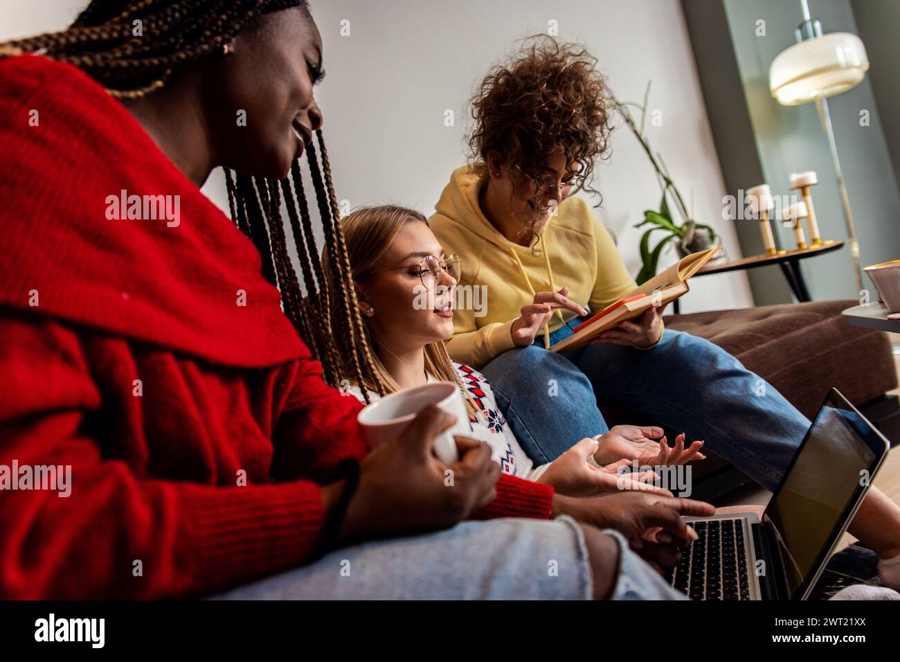 Diverse studentesse di gruppo che imparano a casa utilizzando il laptop e libri per la ricerca. Foto Stock