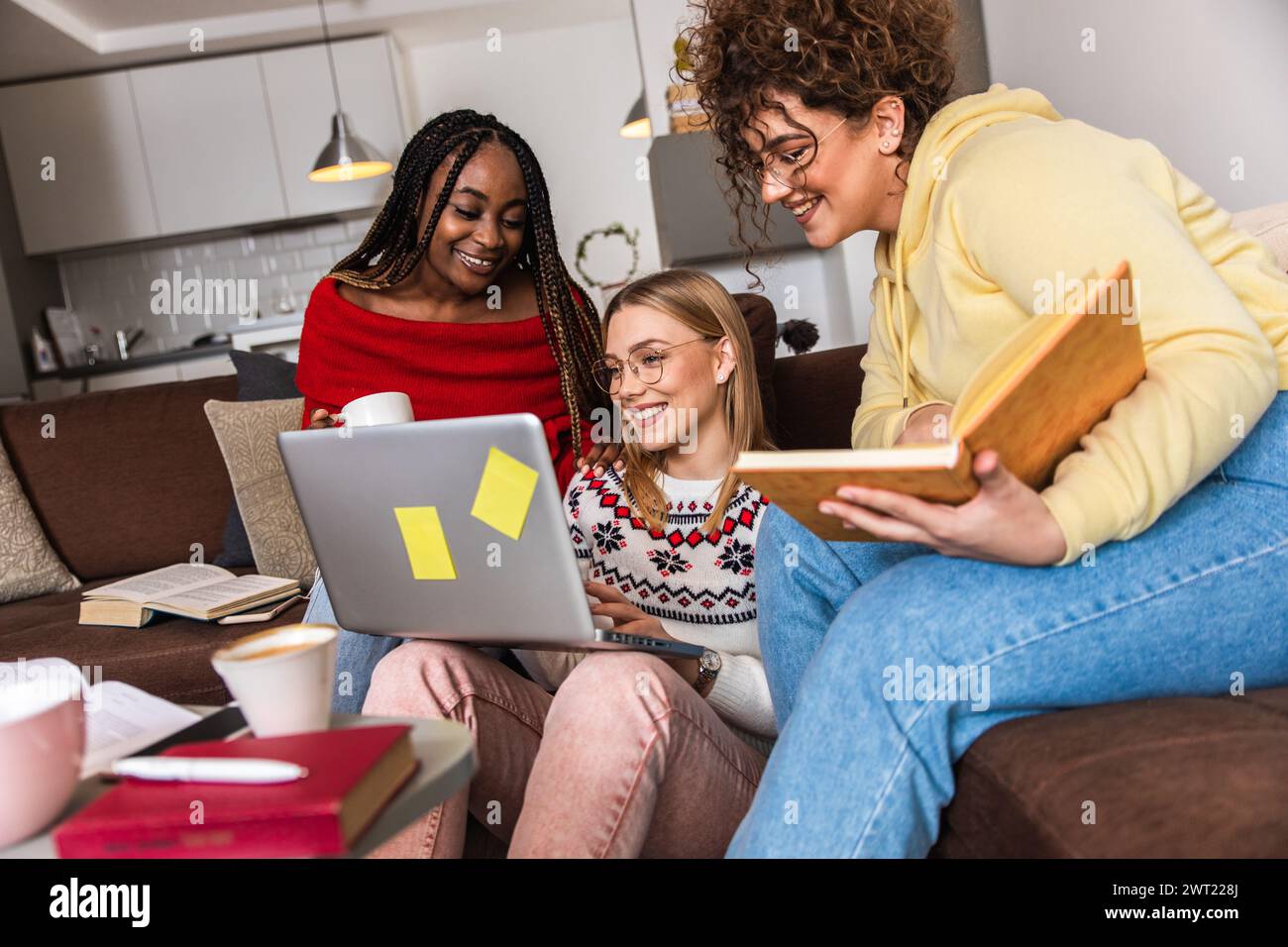 Diverse studentesse di gruppo che imparano a casa utilizzando il laptop e libri per la ricerca. Foto Stock