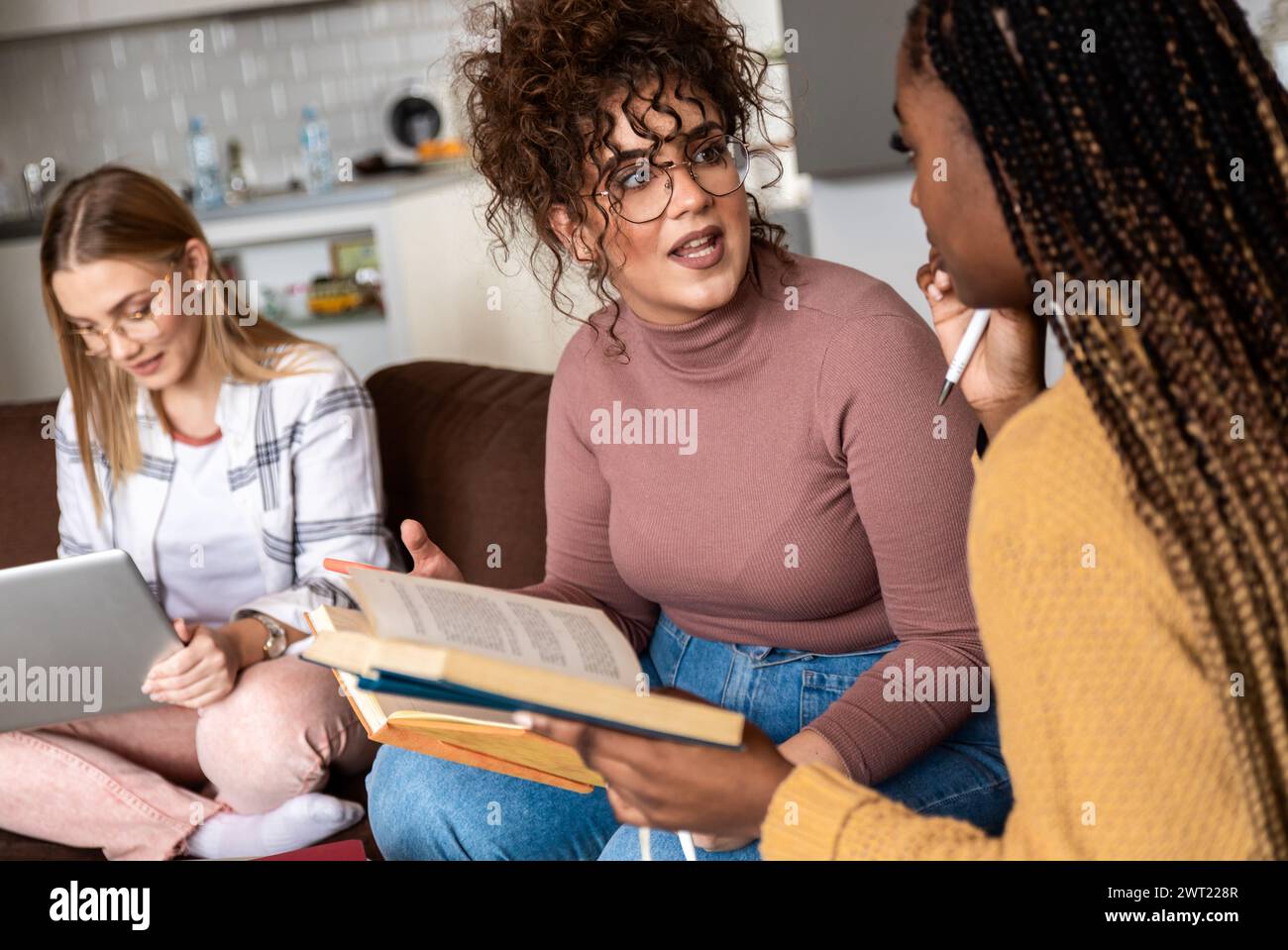 Diverse studentesse di gruppo che imparano a casa utilizzando il laptop e libri per la ricerca. Foto Stock