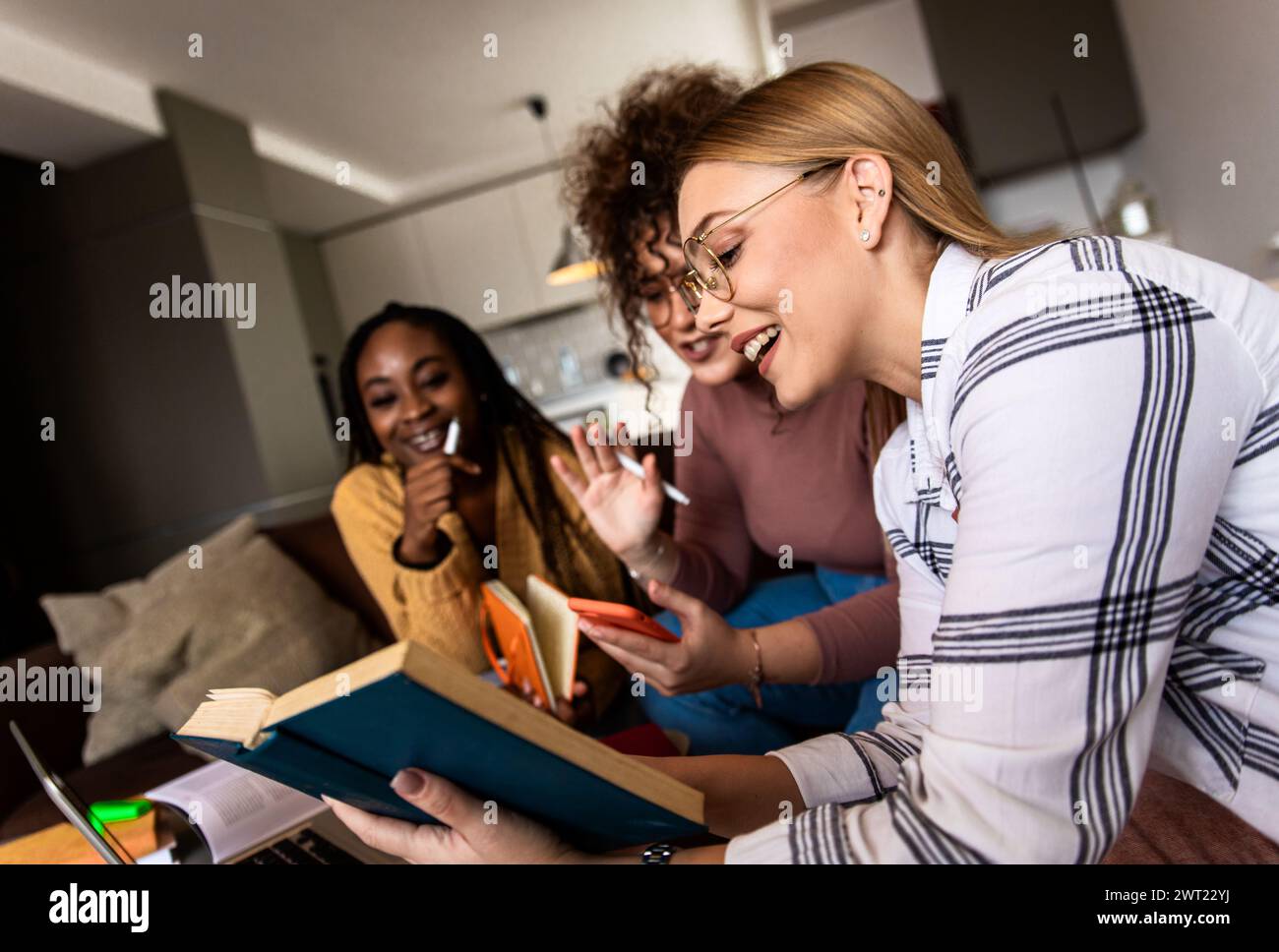 Diverse studentesse di gruppo che imparano a casa utilizzando il laptop e libri per la ricerca. Foto Stock