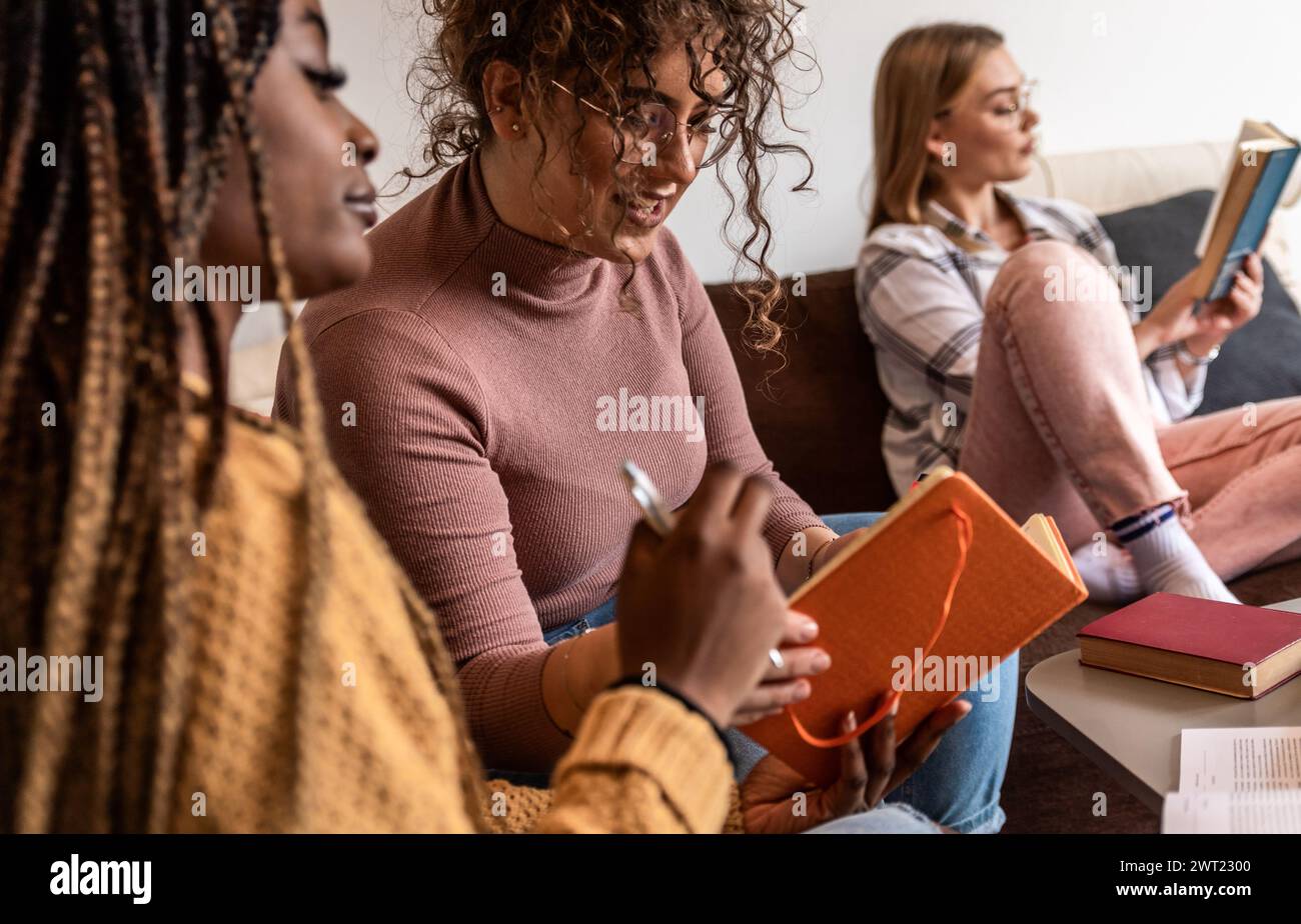 Diverse studentesse di gruppo che imparano a casa utilizzando il laptop e libri per la ricerca. Foto Stock