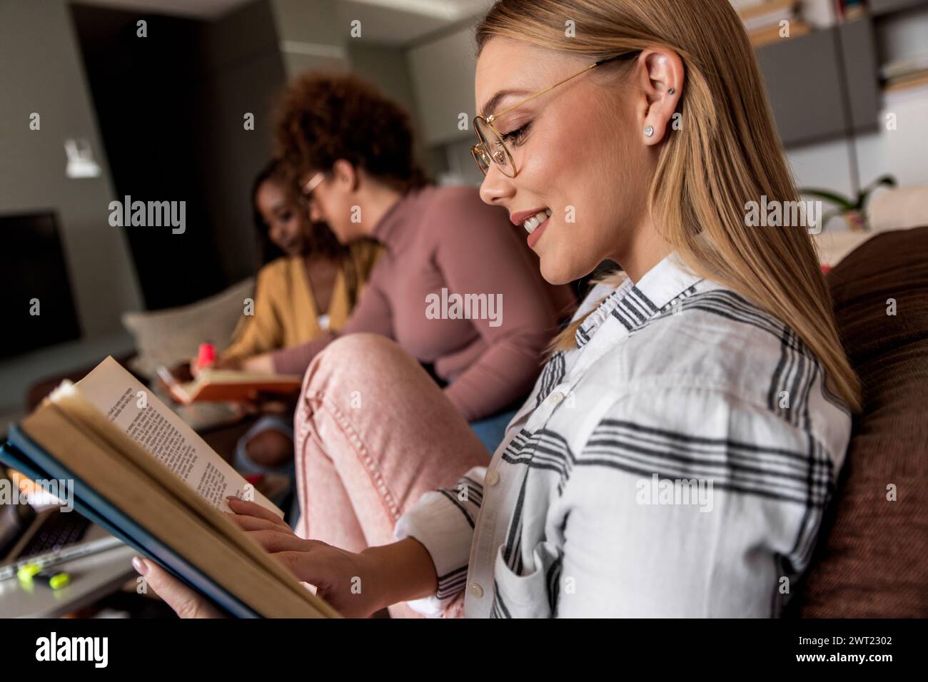 Diverse studentesse di gruppo che imparano a casa utilizzando il laptop e libri per la ricerca. Foto Stock