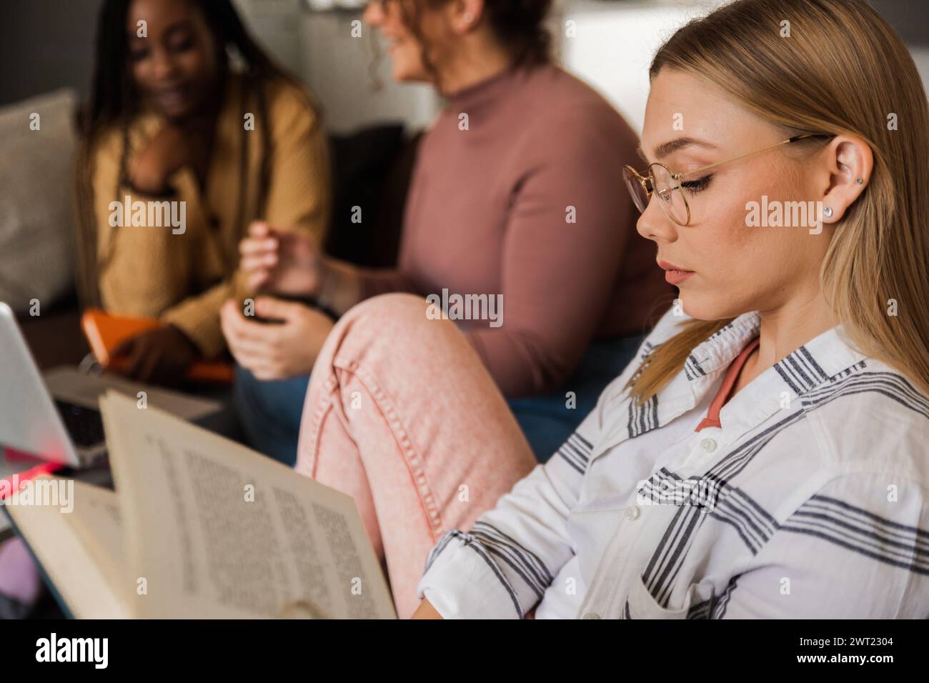 Diverse studentesse di gruppo che imparano a casa utilizzando il laptop e libri per la ricerca. Foto Stock