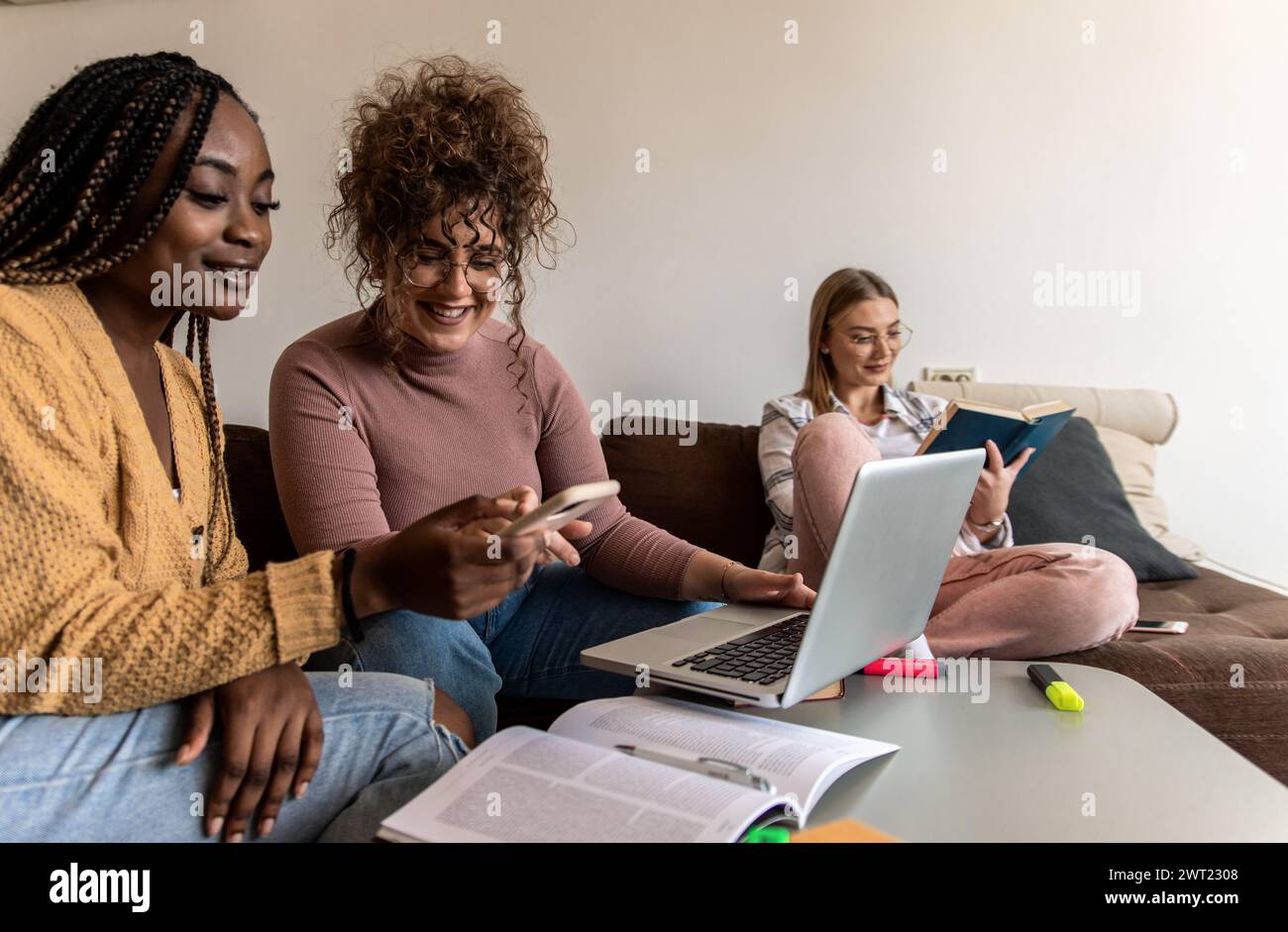 Diverse studentesse di gruppo che imparano a casa utilizzando il laptop e libri per la ricerca. Foto Stock