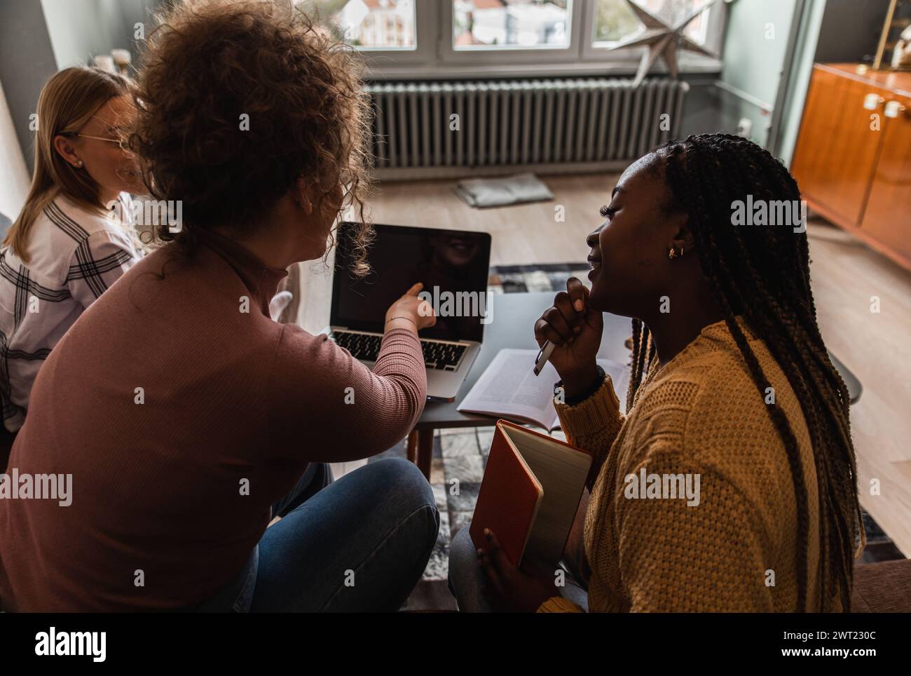 Diverse studentesse di gruppo che imparano a casa utilizzando il laptop e libri per la ricerca. Foto Stock
