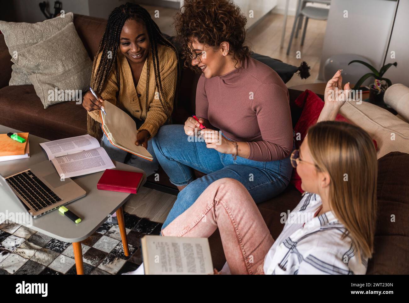 Diverse studentesse di gruppo che imparano a casa utilizzando il laptop e libri per la ricerca. Foto Stock
