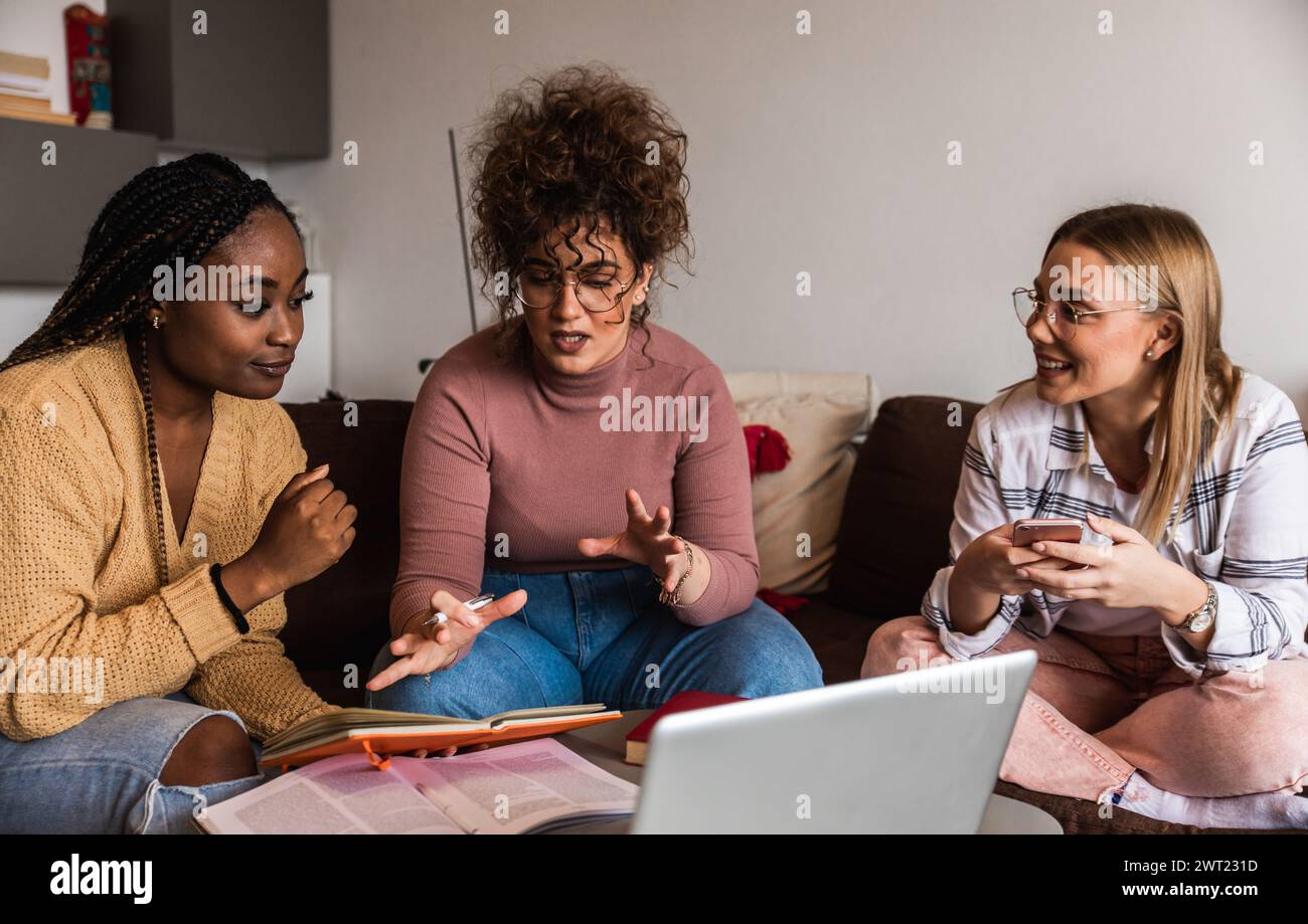 Diverse studentesse di gruppo che imparano a casa utilizzando il laptop e libri per la ricerca. Foto Stock