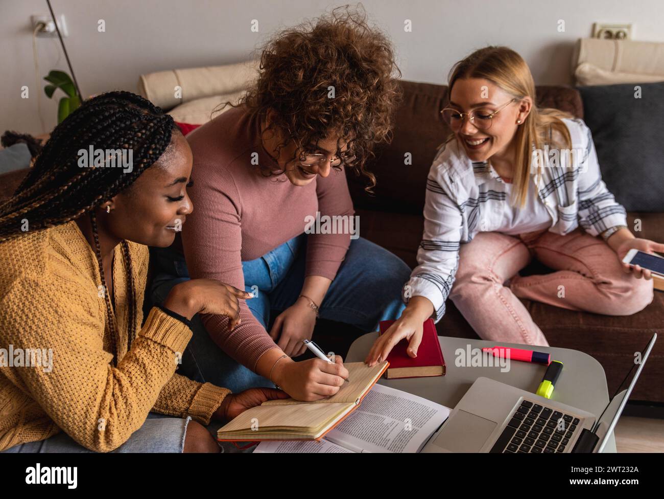 Diverse studentesse di gruppo che imparano a casa utilizzando il laptop e libri per la ricerca. Foto Stock