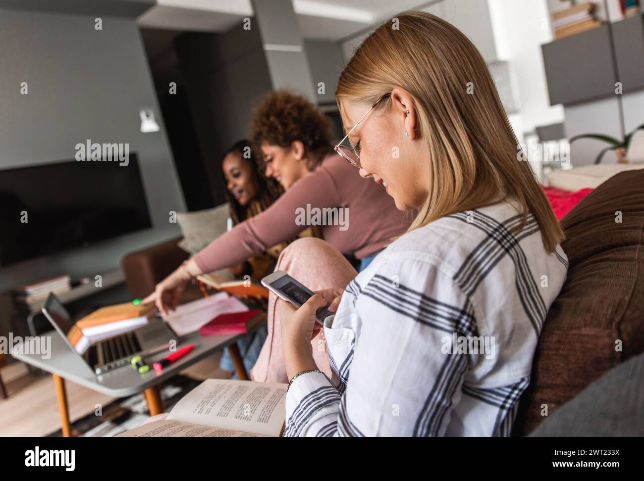 Diverse studentesse di gruppo che imparano a casa utilizzando il laptop e libri per la ricerca. Foto Stock