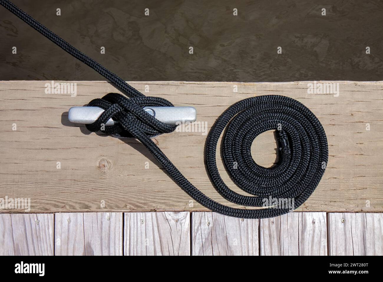 Una fune di ormeggio nera con un'estremità annodata legata intorno a una tacca su un molo di legno. Foto Stock