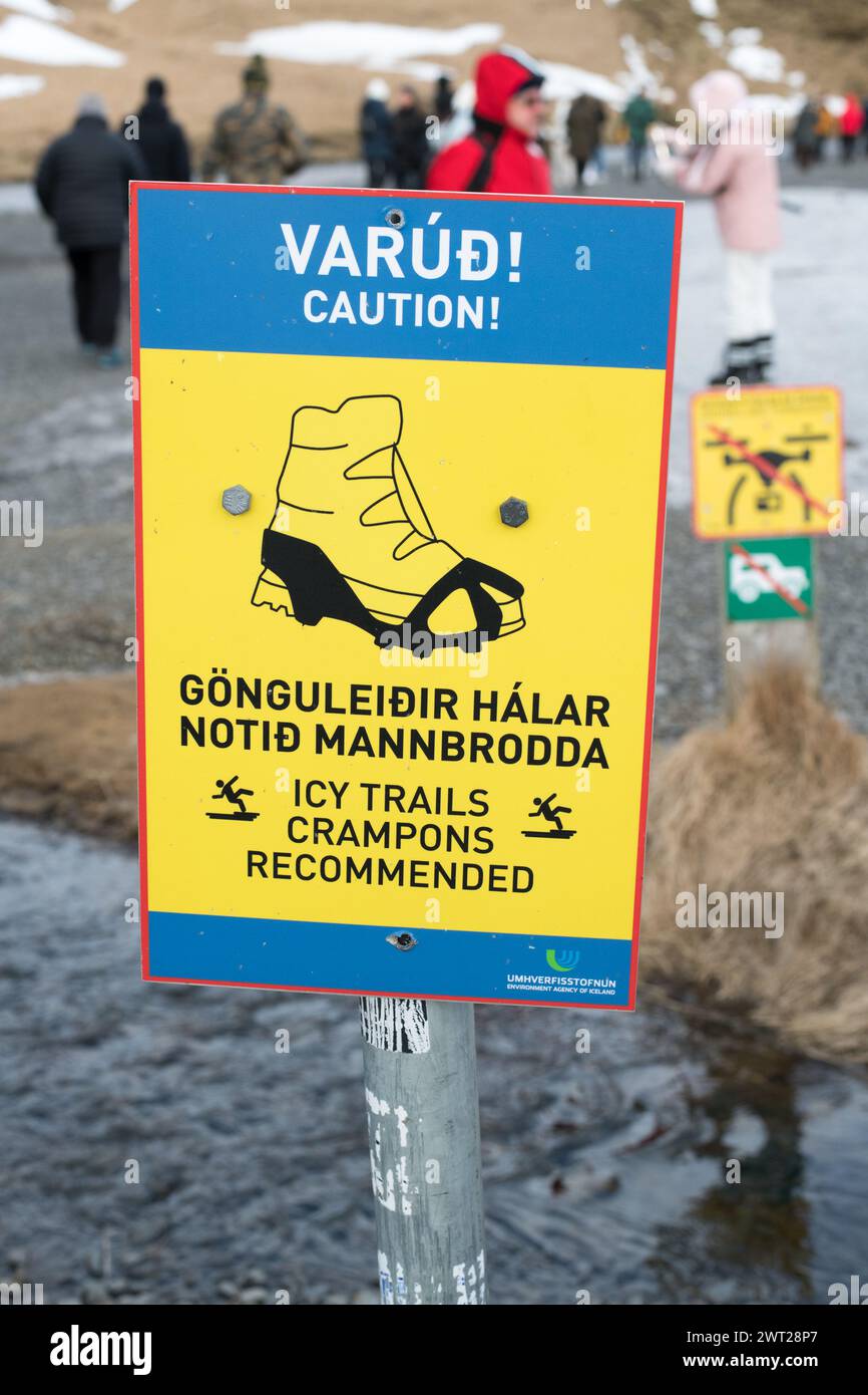 Cartello di avvertimento in inglese e islandese che indica che è necessario prestare attenzione a causa del sentiero ghiacciato e che sono consigliati ramponi. Nessun droni autorizzato ad accedere in background. Foto Stock