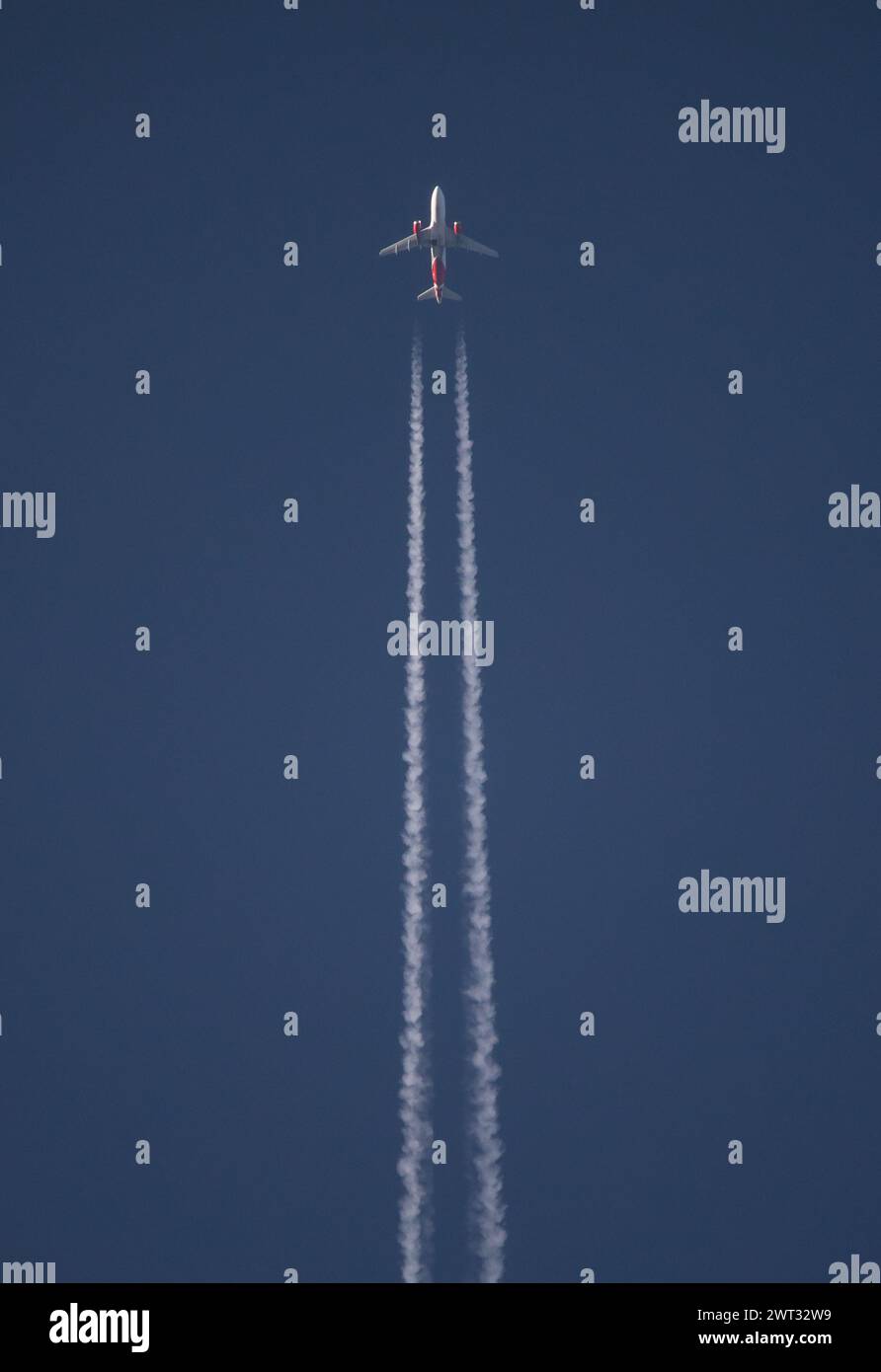 Un aereo di linea commerciale ad alta quota vola in un cielo blu profondo al tramonto con i contrafforti Foto Stock