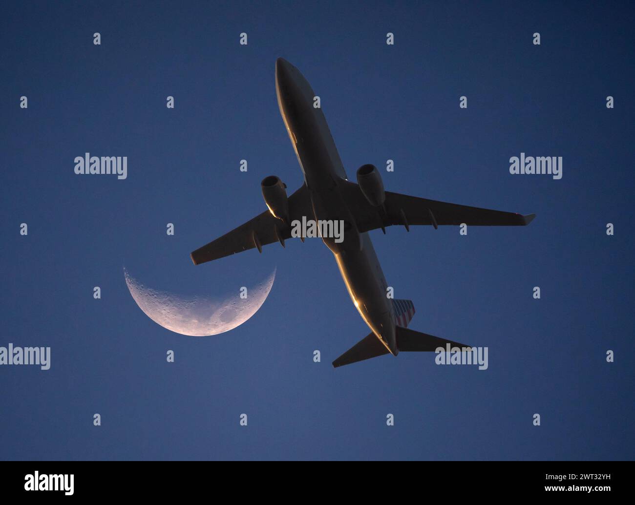Un aereo di linea commerciale a bassa quota passa da una luna crescente al tramonto. Foto Stock
