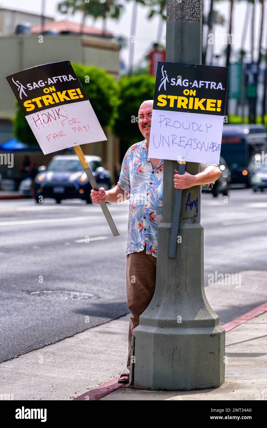 Un attore SAG-AFTRA tiene due cartelli mentre si trova di fronte al traffico vicino alla linea del picchetto durante lo sciopero degli scrittori e degli attori davanti alla Paramount Stud Foto Stock