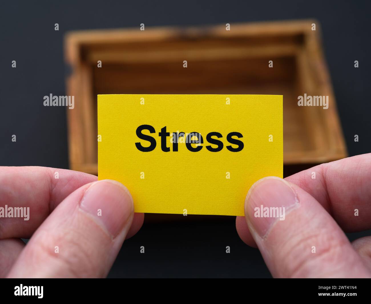 Un uomo che tiene in mano un pezzo di carta gialla con la parola "stress", sopra una piccola scatola di legno vuota. Primo piano. Foto Stock