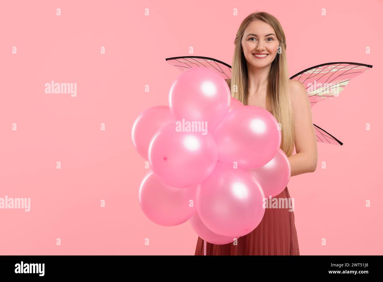 Bella ragazza in costume da fata con ali e palloncini su sfondo rosa, spazio per il testo Foto Stock