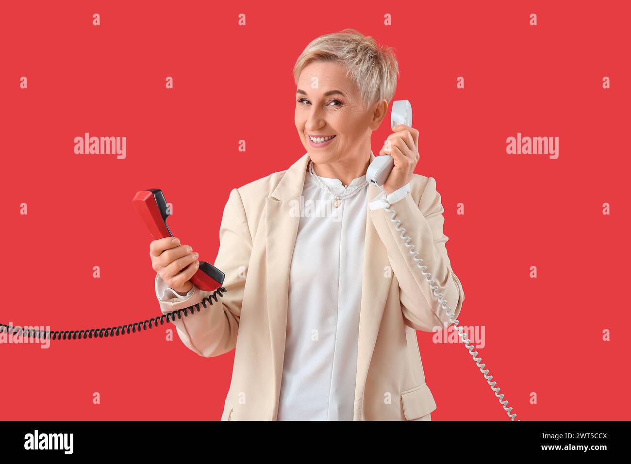 Donna matura con due ricevitori telefonici su sfondo rosso Foto Stock