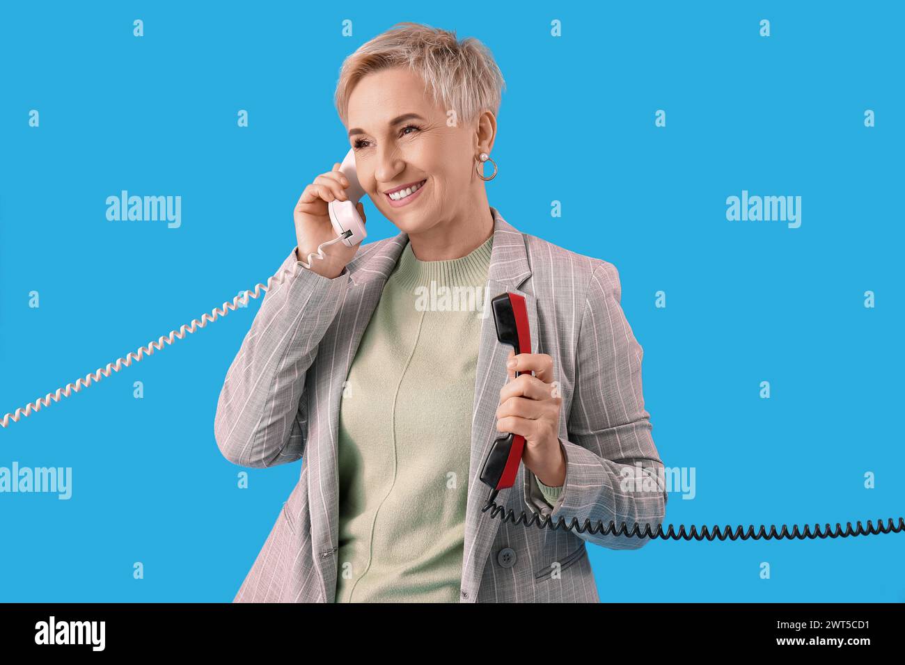 Donna matura con due ricevitori telefonici su sfondo azzurro Foto Stock