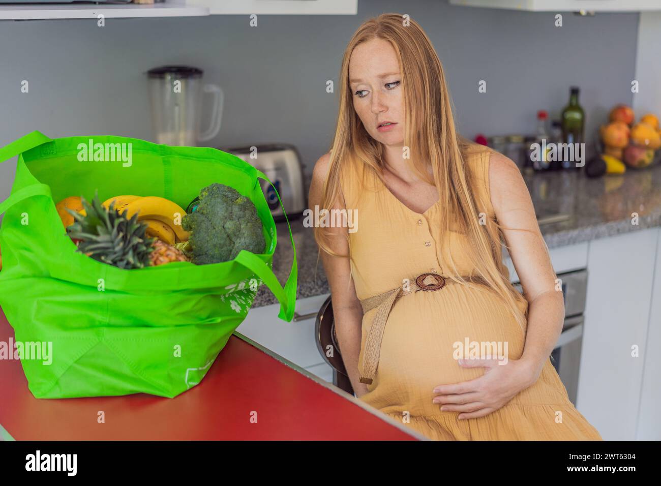 Esausta ma resiliente, una donna incinta prova stanchezza dopo aver portato a casa una grossa borsa di generi alimentari, dimostrando la sua dedizione a fornire Foto Stock