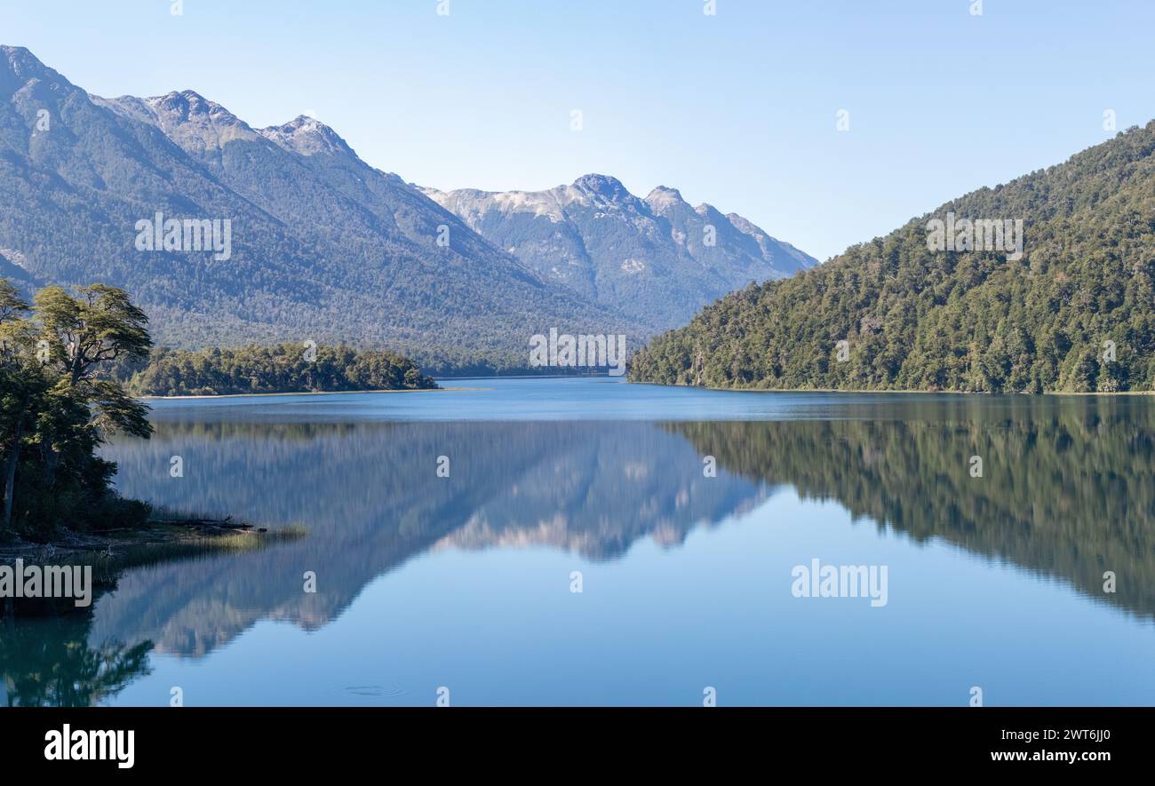 Tranquilla e rilassante vista orizzontale della catena montuosa piena di fitte foreste che si riflettono sulla carta da parati cristallina di un lago Foto Stock