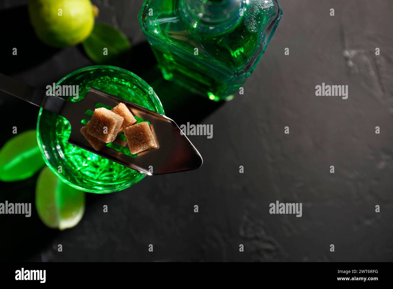 Absinthe, cucchiaio, zucchero di canna e lime sul tavolo nero, vista dall'alto con spazio per il testo. Bevanda alcolica Foto Stock