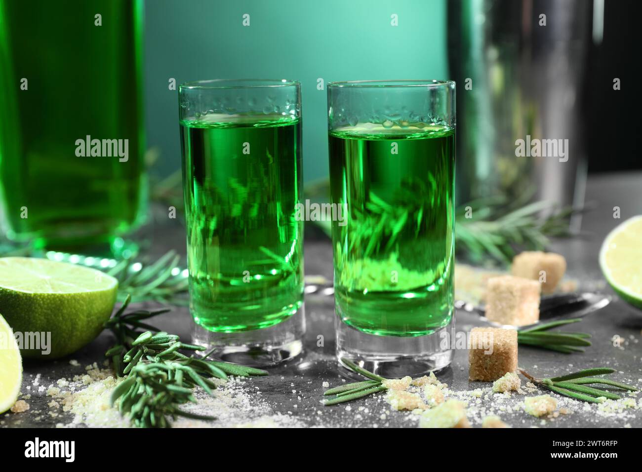 Absinthe in bicchieri da shot, zucchero di canna, rosmarino e lime su tavolo grigio, primo piano. Bevanda alcolica Foto Stock