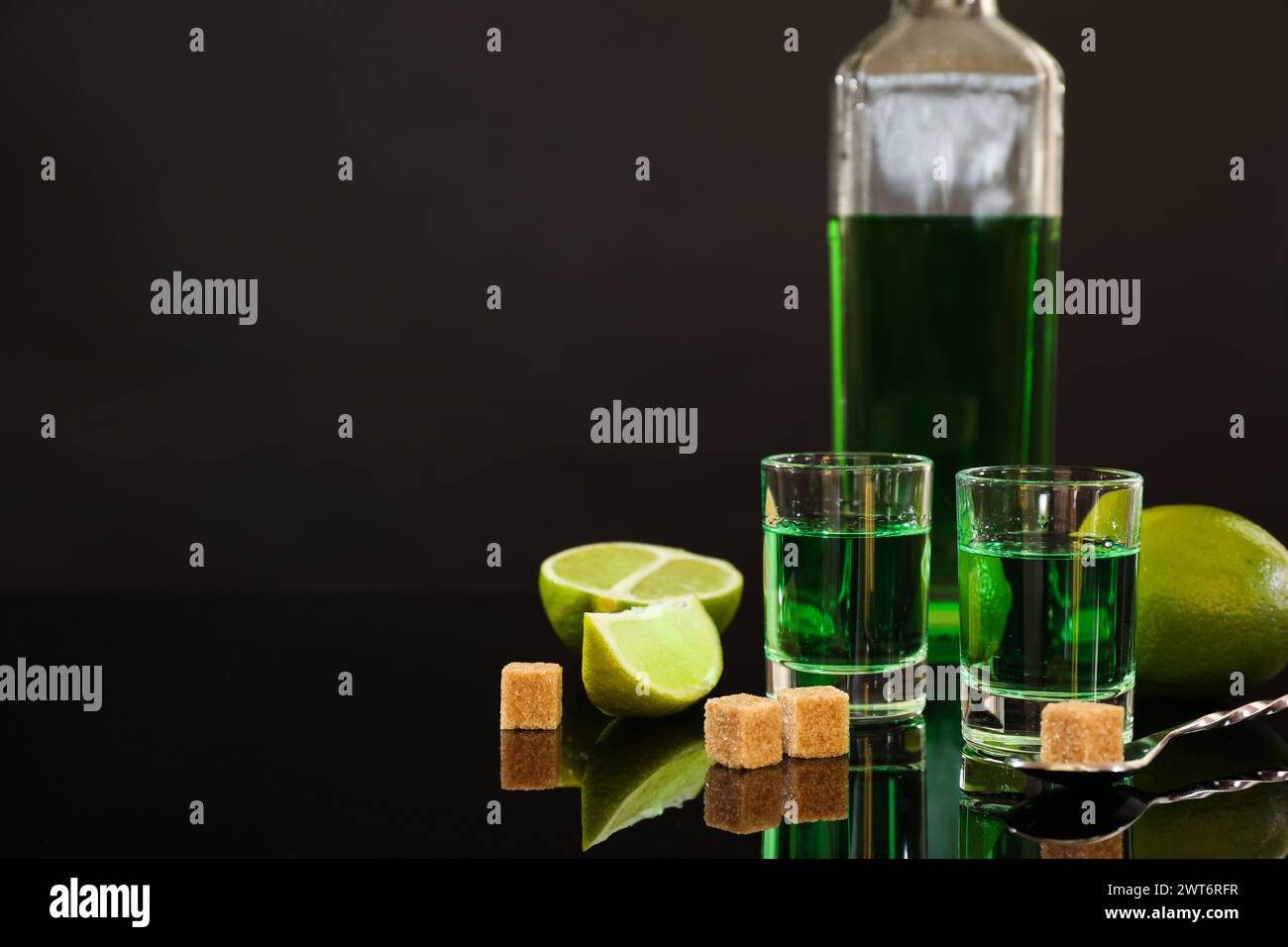 Absinthe in bicchieri da shot, zucchero di canna, lime e cucchiaio sul tavolo a specchio, spazio per il testo. Bevanda alcolica Foto Stock