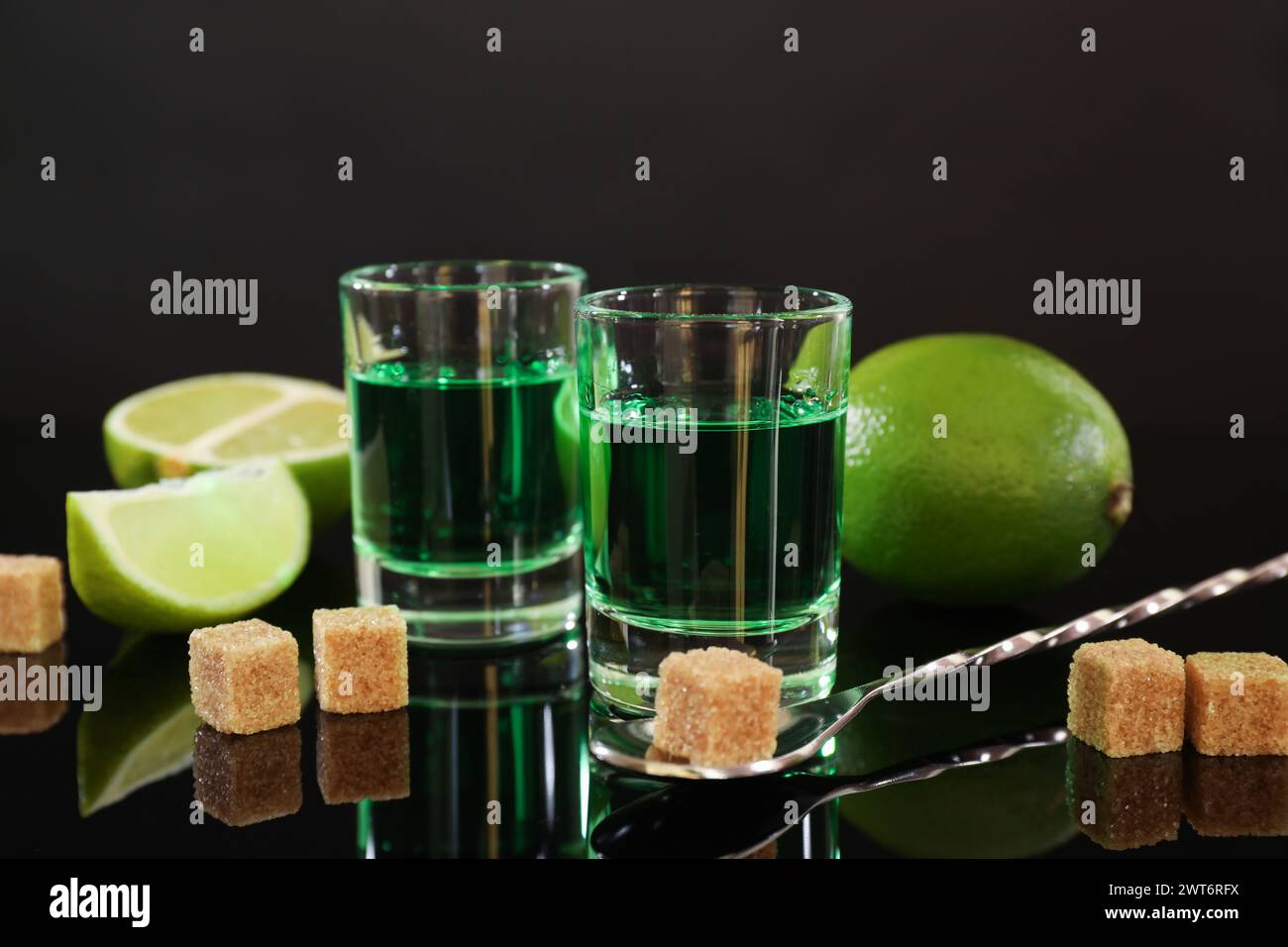 Absinthe in bicchieri da shot, zucchero di canna, lime e cucchiaio sul tavolo a specchio. Bevanda alcolica Foto Stock