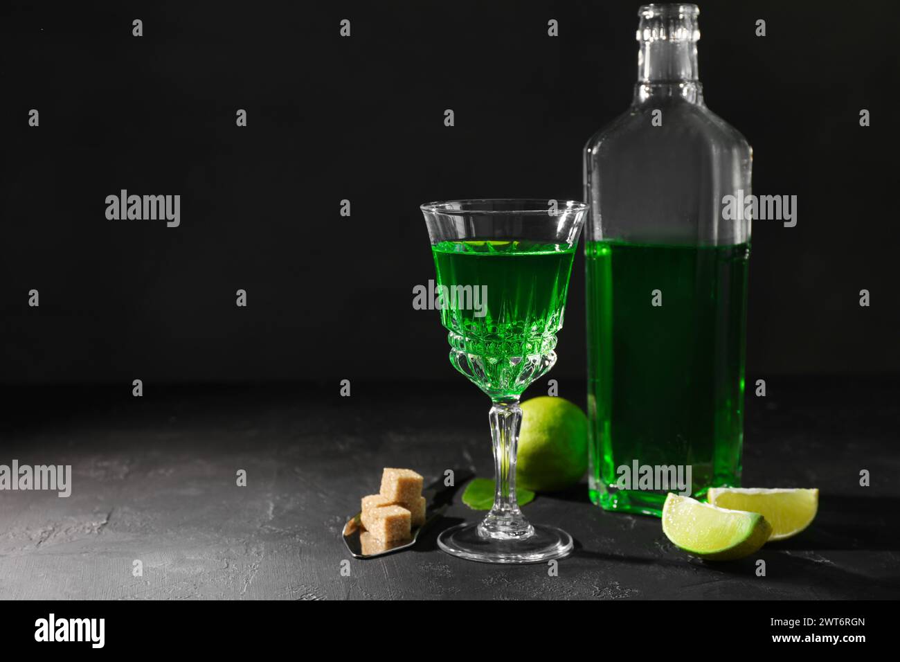 Absinthe, cucchiaio, zucchero di canna e lime sul tavolo nero, spazio per il testo. Bevanda alcolica Foto Stock