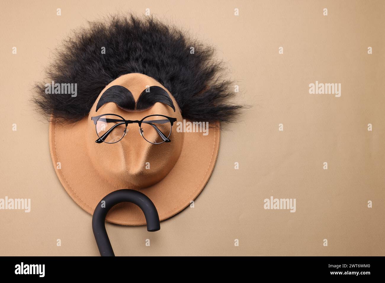 Il viso dell'uomo è fatto di capelli artificiali, sopracciglia, occhiali e cappello su sfondo beige, vista dall'alto. Spazio per il testo Foto Stock