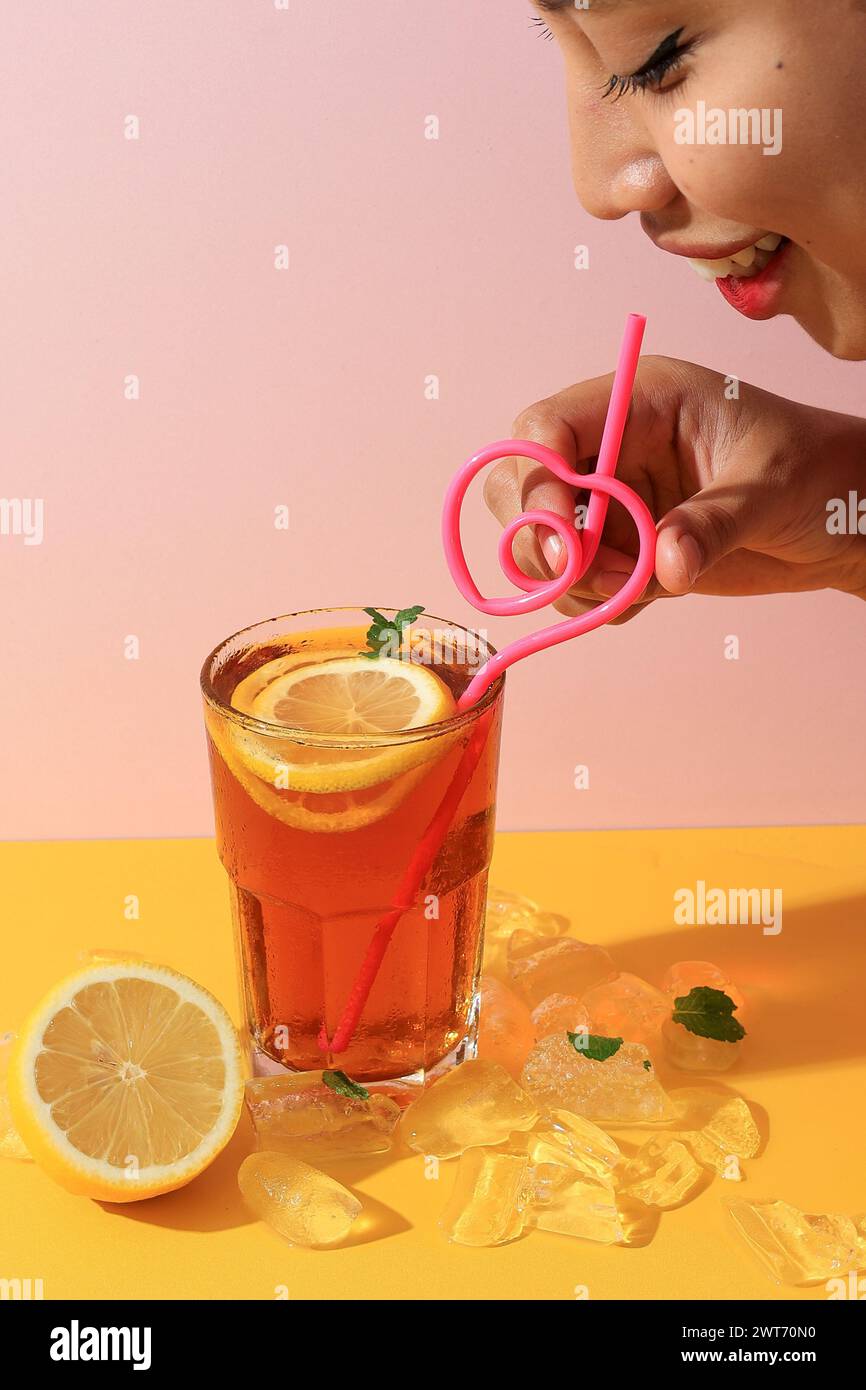 La femmina asiatica beve tè al limone di ghiaccio con paglia rosa a forma di cuore Foto Stock